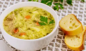 Aromaticzna zupa wiosenna z kawałkami kurczaka, ziemniaków i marchewki, posypana świeżym koperkiem. Obok kromki chleba.