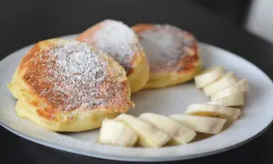 Puszyste, szybkie placuszki na śniadanie posypane cukrem pudrem, obok plasterki banana. Idealne na dobry początek dnia.