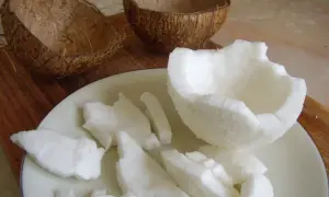 Jak otworzyć kokos? Połówki skorupy i białe kawałki miąższu na talerzu.