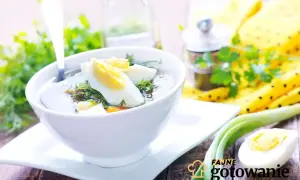 Aromaticzna zupa koperkowa z jajkiem i zieloną cebulką, podana w białej miseczce na drewnianym stole.