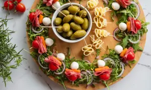 Idealne przekąski na ognisko: szaszłyki z pomidorkami, mozzarellą, salami i marchewką, a obok miseczka oliwek i serowe zawijasy.