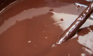 Gładki, błyszczący ganache czekoladowy w misce, z widoczną drewnianą łyżką zanurzoną w jego aksamitnej masie.