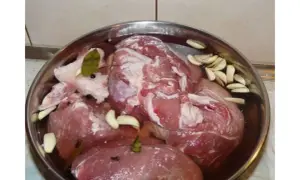 Mięso do peklowania szynki na mokro w metalowej misce z czosnkiem, liściem laurowym i ziarnami pieprzu.