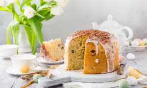 Pyszna babka panettone z lukrem i czekoladą, ozdobiona wielkanocnymi pisankami i białymi tulipanami.
