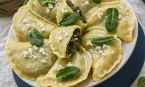 Pyszne pierogi ze szpinakiem i fetą, posypane świeżymi listkami i białym serem. Idealne z czymś lekkim!