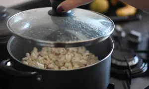 Ręka podnosi pokrywkę garnka, odsłaniając pyszny, świeżo zrobiony popcorn. Idealny sposób, jak zrobić popcorn na wieczór filmowy.