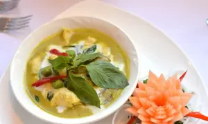 Zielony curry z kurczakiem, podany z bazylią i papryczką chili. Obok ozdobna rzeźba z marchewki.