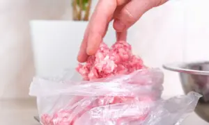 Ręka nakłada mięso mielone do woreczka, przygotowując je do mrożenia. Tak, mięso mielone można mrozić.