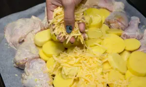 Ręka sypie startym serem na kurczaka i ziemniaki. Pyszny obiad z piekarnika gotowy do pieczenia.
