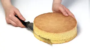 Ręce kroją biszkopt nożem, przygotowując go do dalszych etapów przepisu na tort.