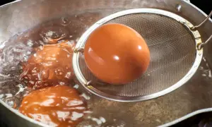 Jajka w trakcie gotowania w garnku. Jedno jajko jest wyjmowane sitkiem.