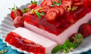 Pyszny deser z truskawkami i galaretką, ozdobiony listkami mięty i pistacjami. Idealny na letnie popołudnie.