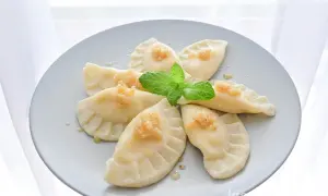 Sześć pierogów na słodko z musem jabłkowym i miętą na szarym talerzu.