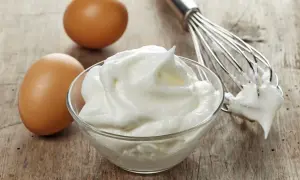 Ubijane białka jaj w misce, obok jajka i trzepaczka.