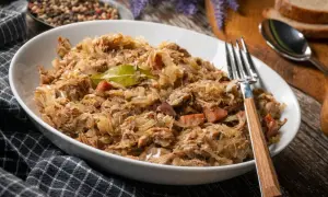 Pyszny bigos w białej misce, z widelcem. Zastanawiasz się, ile może stać bigos w lodówce? Nawet kilka dni, a smakuje coraz lepiej!