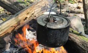 Czajnik wisi nad ogniskiem, gotując pyszne dania z ogniska. Płomienie tańczą pod garnkiem, tworząc magiczną atmosferę.