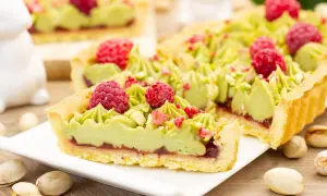 Pyszny mazurek pistacjowy z malinami i chrupiącymi pistacjami, udekorowany zielonym kremem.