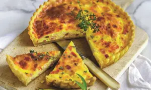 Złocisty quiche lorraine, pokrojony na kawałki, z boczkiem i ziołami, na drewnianej desce.