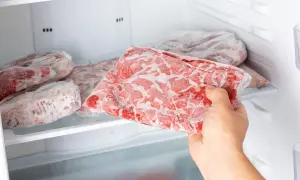Ręka wyjmuje z zamrażarki worek z zamrożonym mięsem. To idealny sposób, w czym mrozić mięso, by zachować jego świeżość.