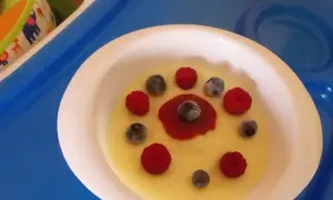 Pyszna kasza manna na wodzie, udekorowana malinami i borówkami, wygląda jak słoneczko na talerzu.