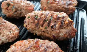 Kebab Adana grillowany na patelni grillowej, z widocznymi kawałkami pomidorów i ziół.