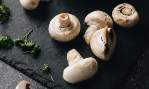 Świeże pieczarki i natka pietruszki na czarnym tle. Zastanawiasz się, czy pieczarki można mrozić? Tak, można je mrozić.