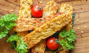 Usmażony tempeh, czyli co to jest? Złociste kawałki fasoli, pomidorki koktajlowe i natka pietruszki na drewnianej desce.