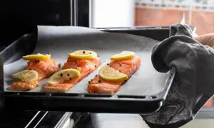 Trzy porcje pieczonego łososia w piekarniku, doprawione cytryną i pieprzem, gotowe do pieczenia.