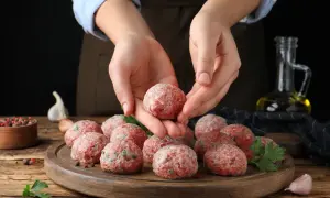 Dłonie formują kotlety mielone bez jajka i bułki. Na desce leżą gotowe do smażenia klopsiki, obok czosnek i przyprawy.