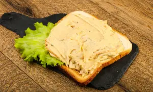 Chleb tostowy z kremową pastą na kanapki i liściem sałaty na czarnej desce.