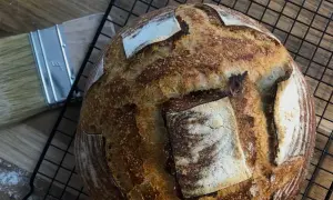 Złocisty, chrupiący chleb pszenny na zakwasie, gotowy do krojenia. Obok pędzel do pieczenia.