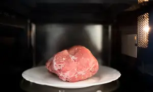 Zamrożony kawałek mięsa na talerzu w mikrofalówce. Szybkie rozmrażanie mięsa w kilka minut.