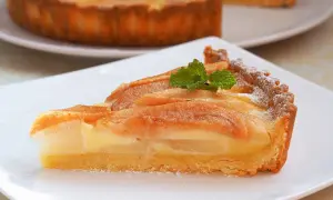 Kawałek pysznej, domowej tarta z gruszką, udekorowana listkiem mięty i posypana cukrem pudrem.