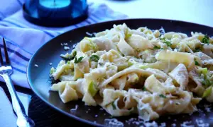 Pyszny makaron z porem, posypany parmezanem i świeżą natką pietruszki, czeka na widelcu.
