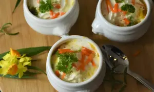 Aksamitna zupa dla dzieci, udekorowana startą marchewką i natką pietruszki. Podana w uroczych białych miseczkach, zachęca do jedzenia.
