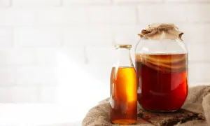 Słoik z ciemnym napojem i widocznym SCOBY, obok butelka z bursztynowym płynem. To jest co to jest kombucha, fermentowany napój.