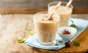 Dwa orzeźwiające **chai latte** z lodem i słomkami, na drewnianym blacie, obok miseczki z anyżem i kardamonem.