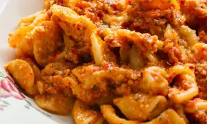 Pyszny makaron z pesto, pełen aromatycznych ziół i pomidorów, podany na talerzu z delikatnym wzorem.