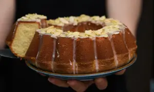 Wilgotna babka wielkanocna, ozdobiona lukrem i płatkami migdałów, prezentuje się apetycznie. Kawałek ciasta został już odcięty.