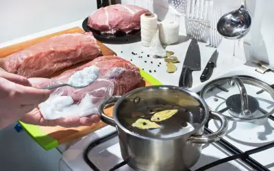 Przygotowania do peklowania na mokro: mięso, sól, przyprawy i garnek z zalewą na kuchence.
