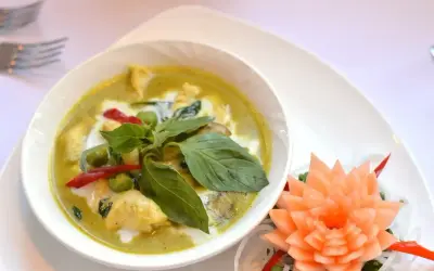Zielony curry z kurczakiem, podany z bazylią i papryczką chili. Obok ozdobna rzeźba z marchewki.