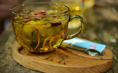 Aromatyczna herbata z dodatkiem imbiru do herbaty, kwiatów i jagód. Podana w szklanej filiżance na drewnianej podstawce.