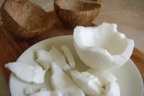 Jak otworzyć kokos? Połówki skorupy i białe kawałki miąższu na talerzu.