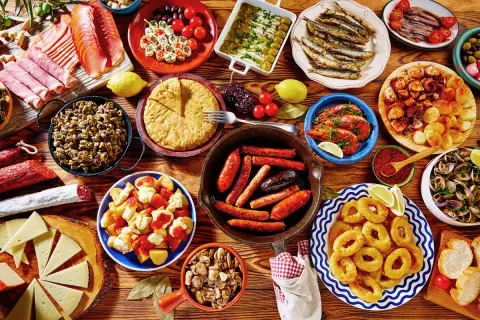 Tapas co to? Kolorowy stół pełen hiszpańskich przekąsek: kiełbaski, krewetki, kalmary, owoce morza, ser, tortilla i wędliny.