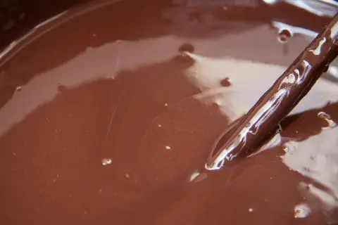 Gładki, błyszczący ganache czekoladowy w misce, z widoczną drewnianą łyżką zanurzoną w jego aksamitnej masie.