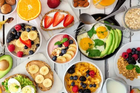 Kolorowe śniadanie dla dzieci: owsianka z owocami, tosty z awokado i jajkiem, płatki z jagodami, smoothie, jajka sadzone z awokado i sok pomarańczowy.
