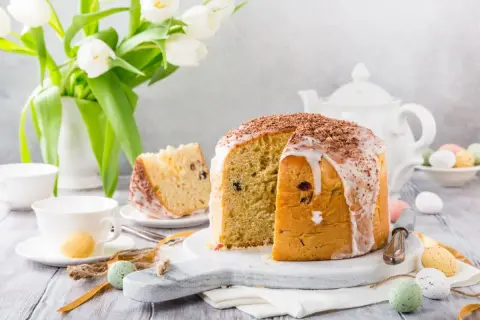 Pyszna babka panettone z lukrem i czekoladą, ozdobiona wielkanocnymi pisankami i białymi tulipanami.