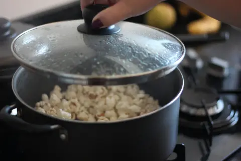 Ręka podnosi pokrywkę garnka, odsłaniając pyszny, świeżo zrobiony popcorn. Idealny sposób, jak zrobić popcorn na wieczór filmowy.
