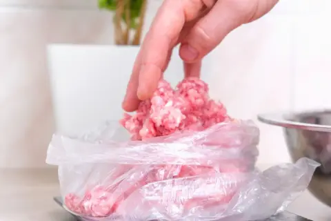 Ręka nakłada mięso mielone do woreczka, przygotowując je do mrożenia. Tak, mięso mielone można mrozić.