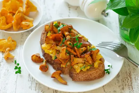 Tost z jajecznicą i kurkami, posypany ziołami. Pyszne danie na śniadanie lub lekki posiłek.